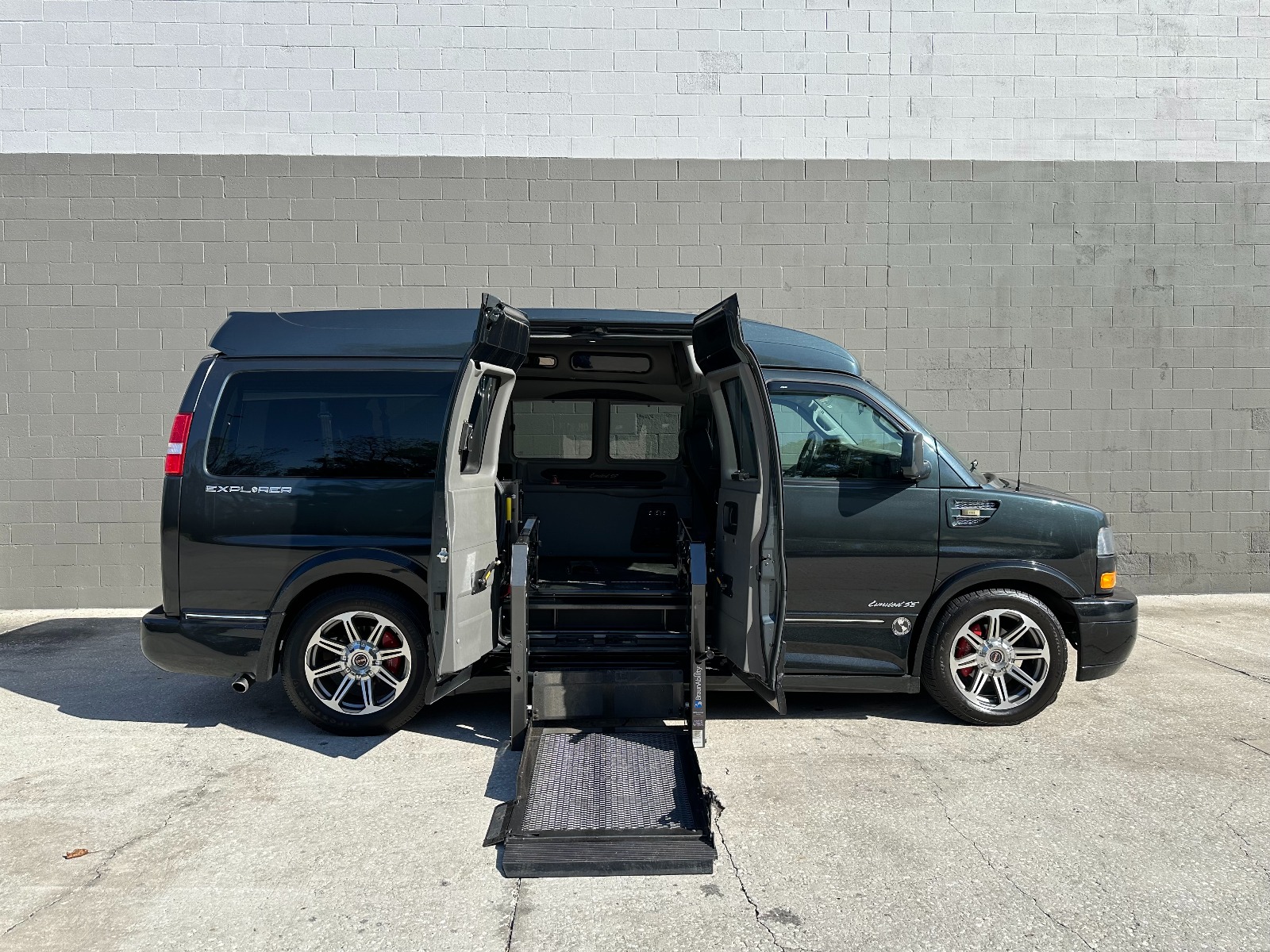 Black GMC Savana Full Size Wheelchair Van with lift deployed from open passenger side barn doors.