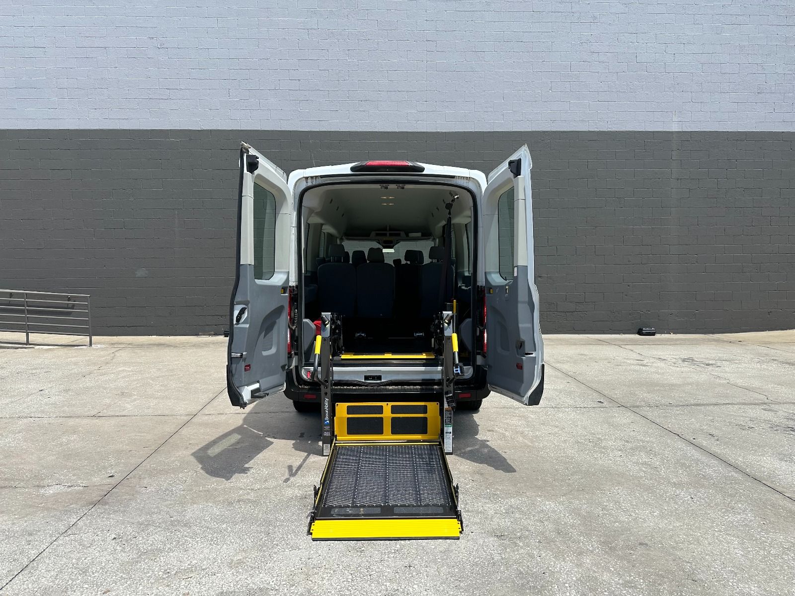 White Ford Transit full size wheelchair van with the wheelchair lift deployed from the open rear barn doors.