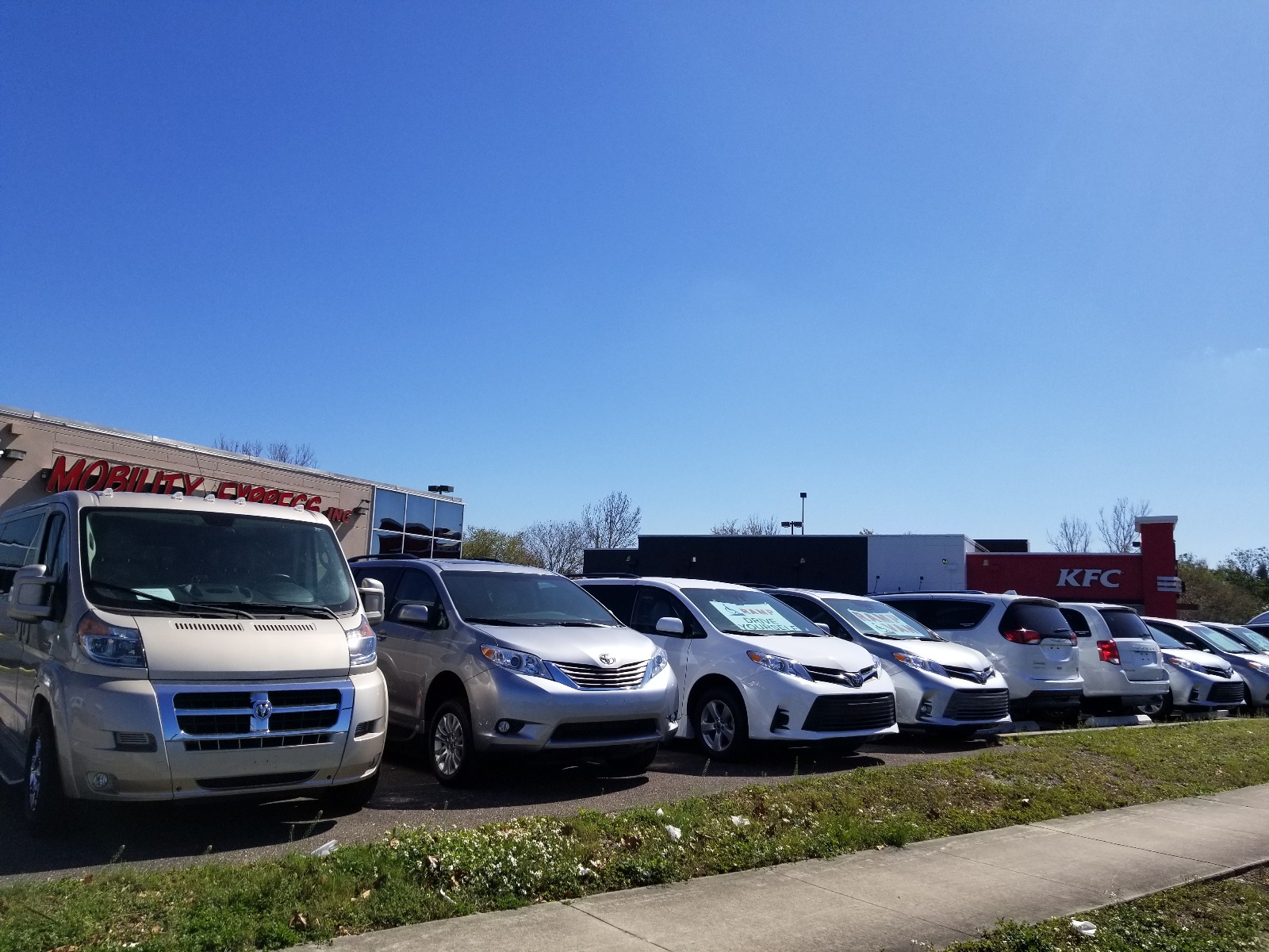 A line of handicap accessible vans parked with most facing forward, in front of a building for the wheelchair van dealer Mobility Express.