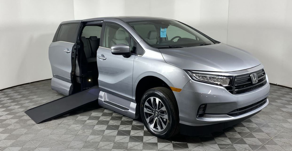 A silver Honda Odyssey with AMS wheelchair van conversion with ramp deployed from open passenger sliding doorway.
