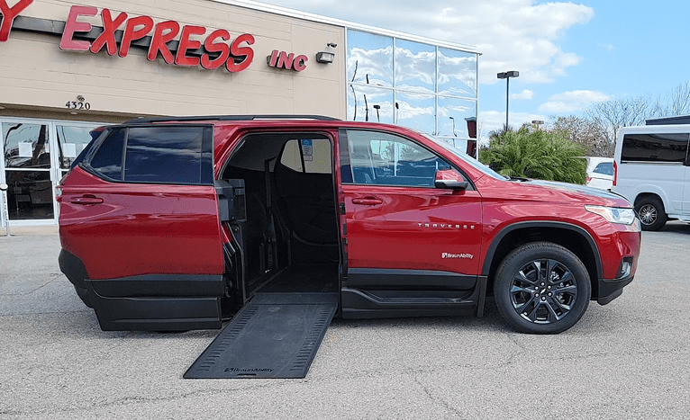 A red wheelchair accessible SUV with the ramp deployed from the open passenger side rear door. There's a building in the background and part of the company's sign is visible. Just the words "Express Inc".