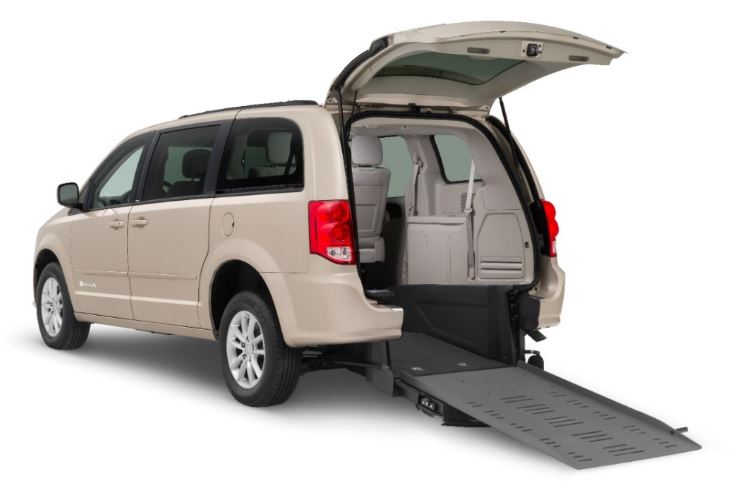 Champagne colored Dodge Grand Caravan with rear entry wheelchair van conversion with ramp deployed from open rear hatch.