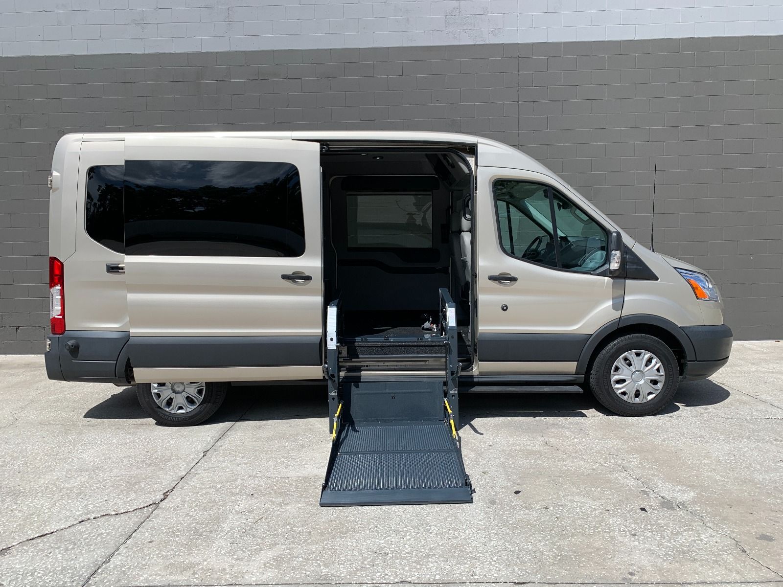 Ford Transit full size wheelchair van with the wheelchair lift deployed from the open passenger side sliding door.